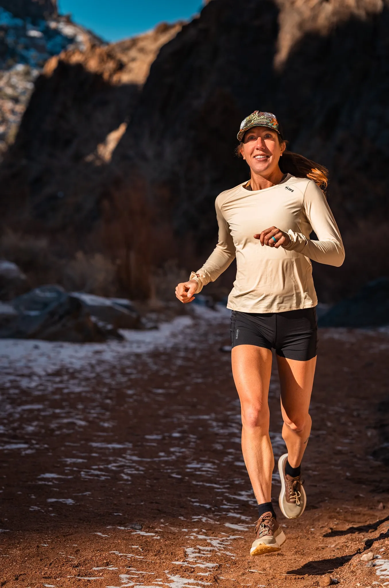 Megan Eckert smiling as she runs along a rocky canyon trail in a cap and long-sleeve top