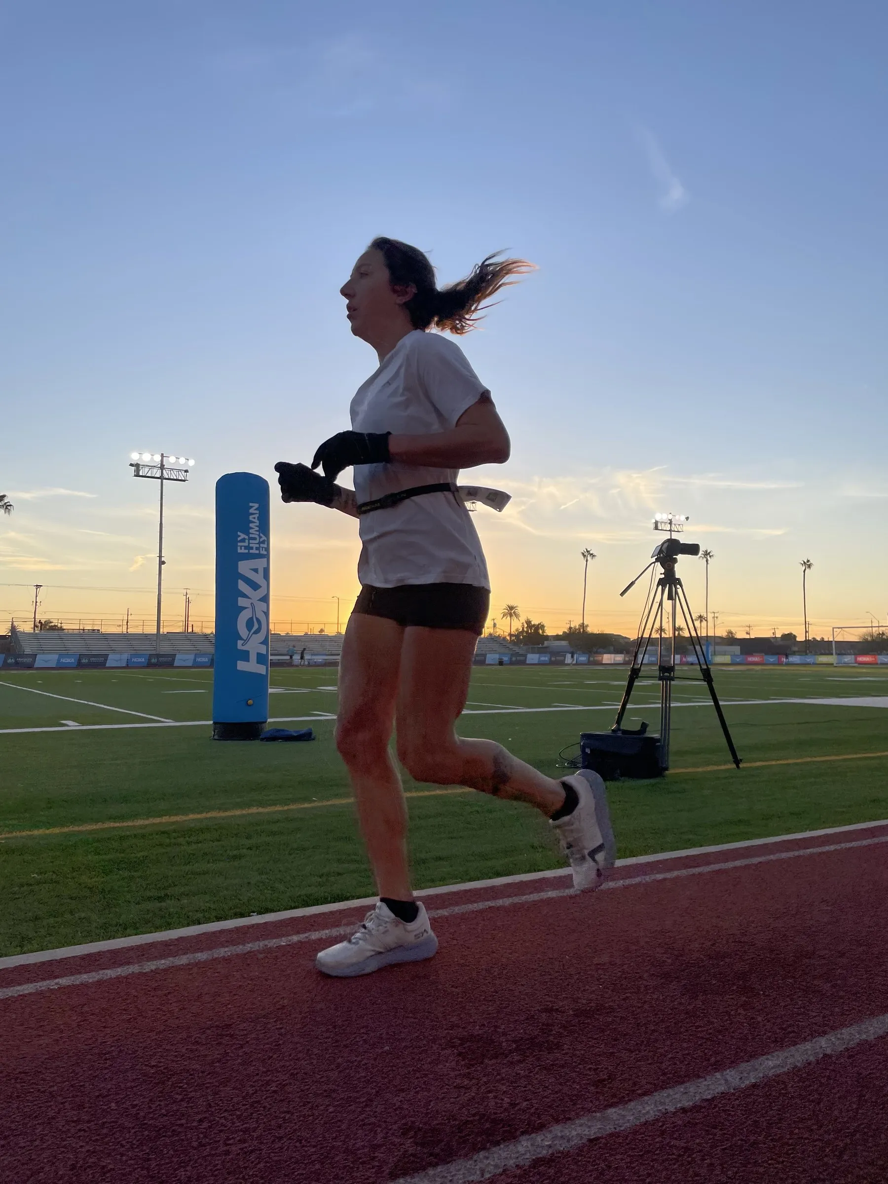 Megan Eckert running on a track at dusk beside a timing tent