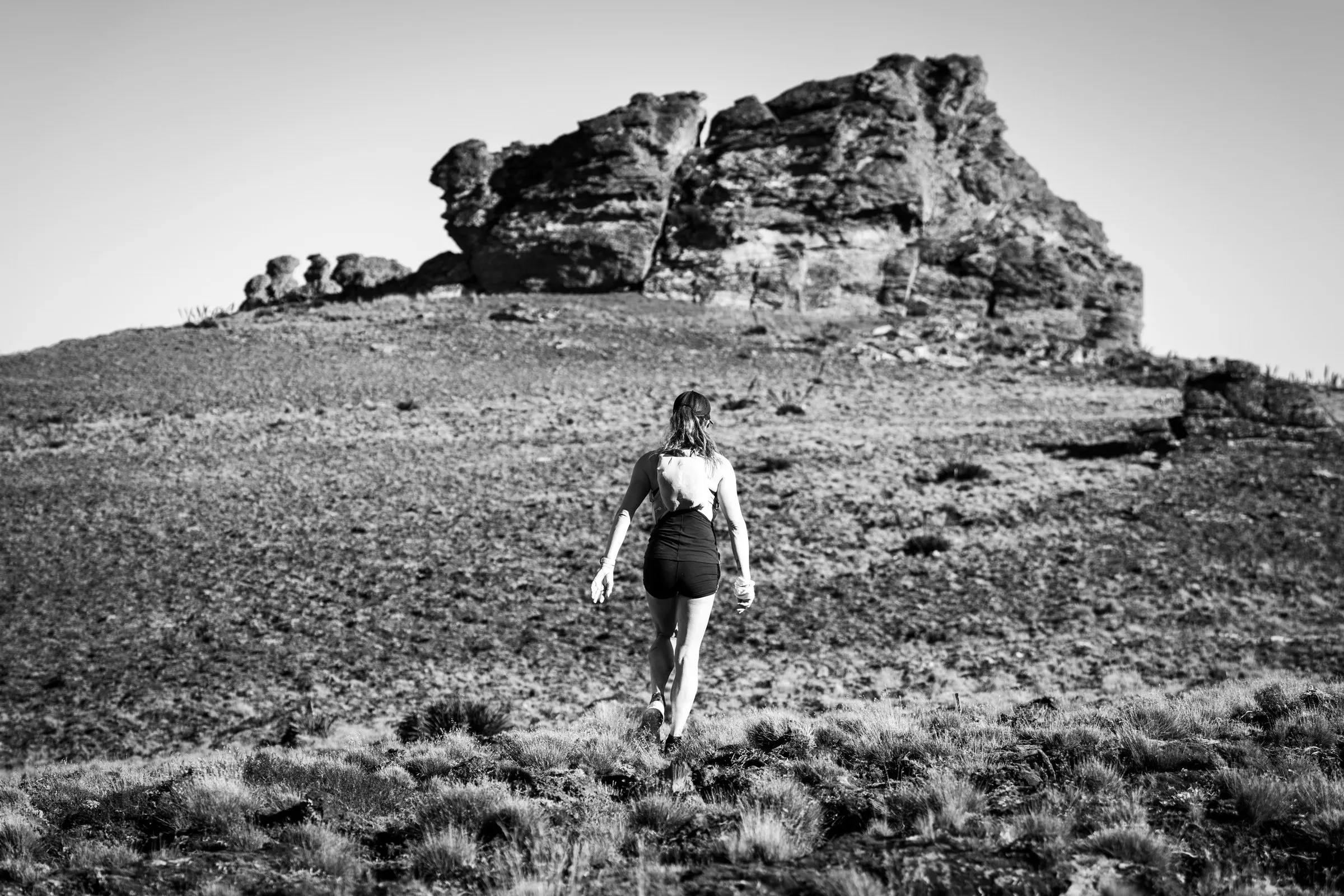 Black-and-white photo of Megan Eckert running toward a rock outcrop on open high country